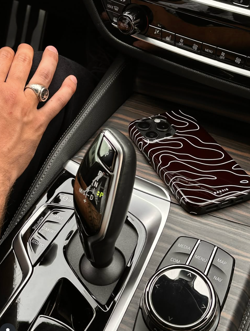 Car interior with gear shift and hand, phone with unique case on wooden surface