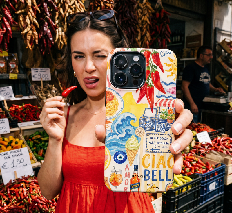 A woman in a red dress holds up a phone case featuring a colorful 'Ciao Amore' Sicilian collage design with illustrations of chili peppers, waves, and local landmarks, set against a busy market background filled with red chilies.